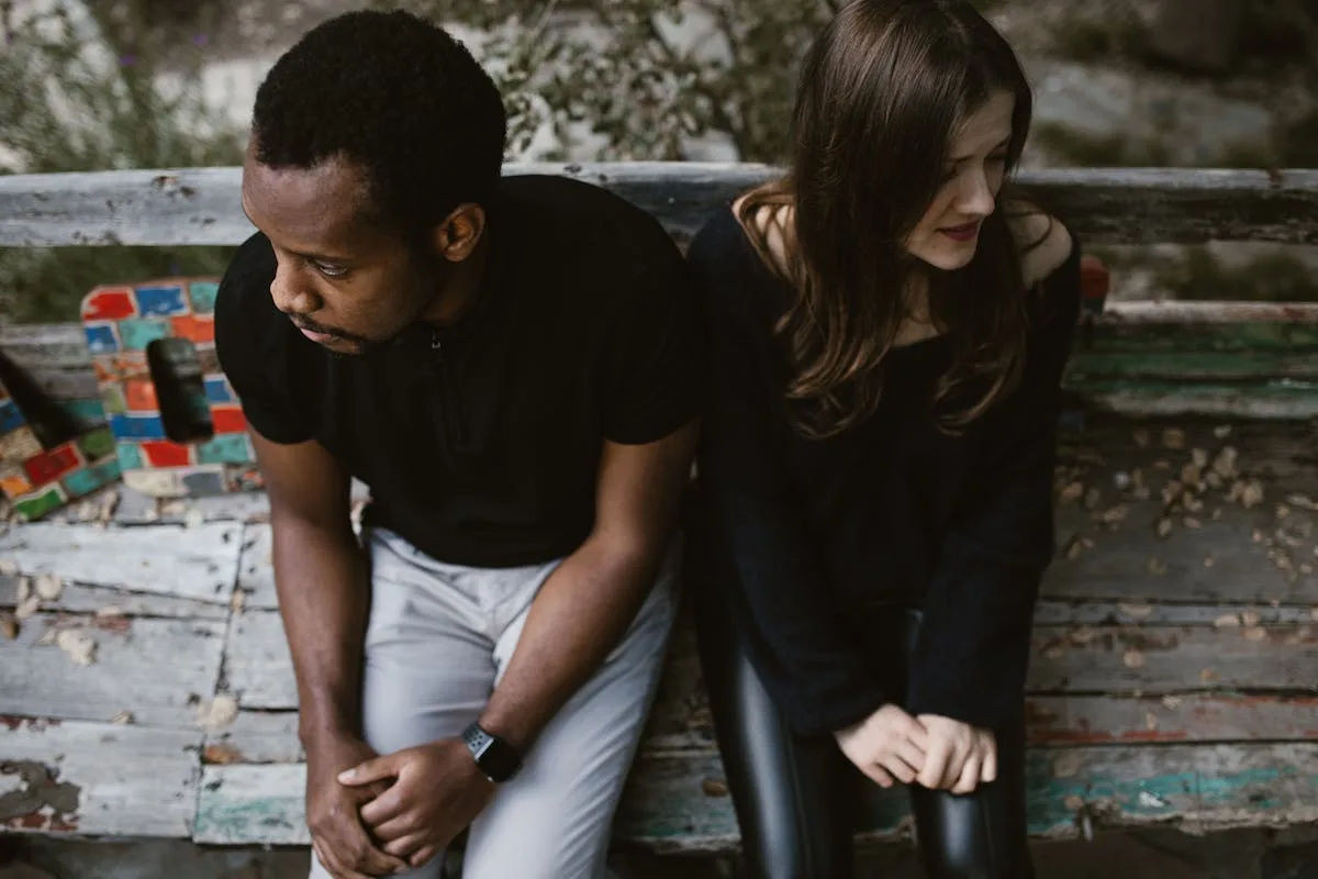 Couple sitting apart, showcasing signs he is emotionally unavailable in a park.