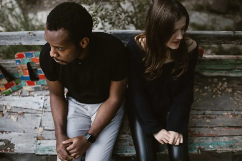Couple sitting apart, showcasing signs he is emotionally unavailable in a park.